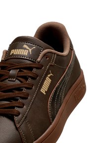 Кафяв маратонка Puma с подходящи връзки, бежови лога Puma на езици и странични части, и текстуриран яка за подкрепа на глезена.