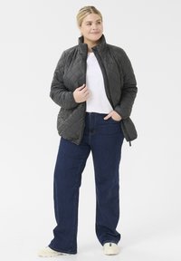 Quilted dark gray jacket with a stand collar, zippered front, and long sleeves, paired with blue denim pants and light sneakers.
