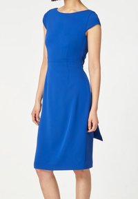 Blå tajt klänning med korta ärmar, knälång fåll och en slät, mjuk tygfinish. Har en subtil sidopaneldetalj.