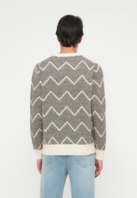 Pletena pulover s čarobnim vzorcem v temno sivi in kremni barvi. Ima okroglo izrez, rebraste manšete in pas. Dolgi rokavi.