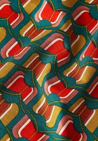 Textil med ett geometriskt mönster i teal, röd, rosa och guld. Ytan är vävd, med släta, böjda former och kontrasterande linjer.