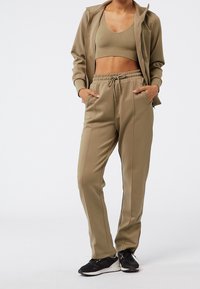 Tvådelat träningsset i dämpad olivgrön, bestående av en zip-up jacka och höga byxor med sidofickor och elastisk midja.