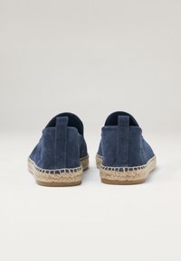 Espadrilles de ante azul marino con suela de yute trenzada, tirador en la parte trasera y una textura suave. Forma redondeada con talón cerrado y lados abiertos.