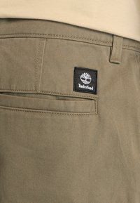 Pantalones caqui fabricados en algodón que cuentan con un bolsillo trasero con un parche del logo negro de Timberland. Corte recto con detalles de costura visibles.