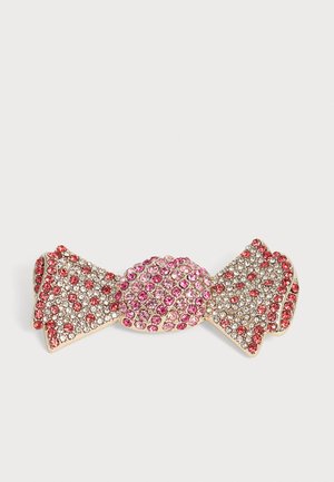 Broche en forme de nœud ornée de strass roses et transparents sur une base dorée, présentée sur un fond blanc.