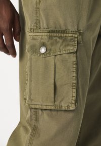 Cargo shorts in een olijfgroene kleur, gemaakt van textuurstof. Beschikt over een grote zak met een zilveren drukknopdetail.