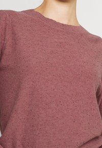 Pullover mit Rundhalsausschnitt in staubigem Rosaton, gefertigt aus weichem Strickstoff, mit einer gesprenkelten Textur und dunklen Flecken durchgehend. Einfaches, entspanntes Design.