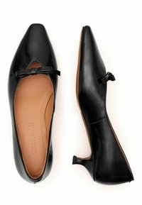 Scarpe nere a tacco basso con punta appuntita, realizzate in materiale sintetico lucido. Presentano un piccolo fiocco decorativo vicino all'arco e una superficie testurizzata.