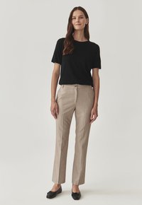 Maglietta nera a maniche corte abbinata a pantaloni beige con righe. I pantaloni hanno una chiusura con bottone e un design a gamba dritta. Ballerine nere.