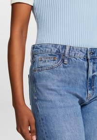 Top de canalé azul claro combinado con unos vaqueros de denim azul desgastado de tiro alto que presentan costuras visibles y un logo sutil en contraste en el bolsillo.