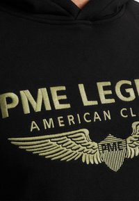 Felpa nera con cappuccio con testo "PME LEGEND" ricamato in oro. Dettagli includono design di ali e scudo, texture liscia.
