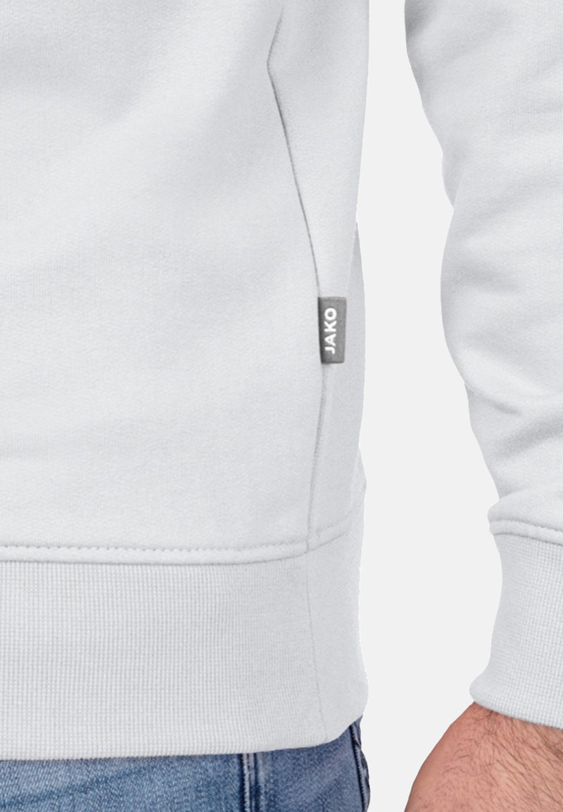 Sweatshirt gris clair en coton doux avec des poignets et un ourlet côtelés. Présente une petite étiquette logo grise sur le côté. Coutures détaillées visibles.