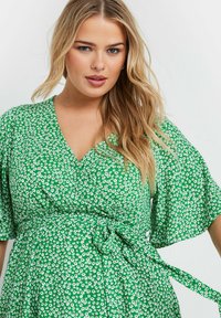 Grön omslagsklänning med ett blommigt mönster i vitt, korta volangärmar, V-ringning och en knytning i midjan.