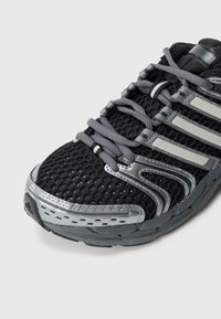 Černá sportovní obuv s horní částí z prodyšné síťoviny, šedými metalickými akcenty a texturovanou podrážkou pro lepší přilnavost. Šněrovadla jsou šedá a mají pevnou špičku.