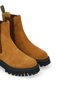 Bottines en daim marron avec des panneaux élastiques sur les côtés, dotées d'une semelle en caoutchouc noir épais avec une profonde bande de roulement et d'une languette à l'arrière.