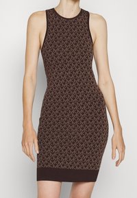 Robe sans manches en tricot marron foncé, avec un motif géométrique en marron clair. Silhouette ajustée avec un ourlet côtelé.