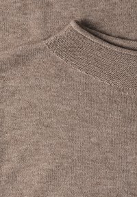 Gros plan d’un pull marron tricoté doux montrant une texture détaillée et un col côtelé.
