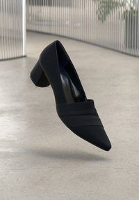 Black high-heeled shoe with a pointed toe, featuring a smooth texture and horizontal stripes across the front. Chunky block heel.
