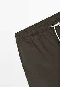 Donkergroene shorts met elastische taille, witte trekkoord en zijzakdetail op een witte achtergrond.