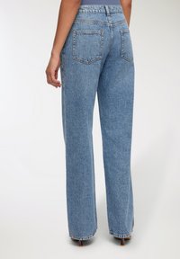 Jeansy z wysokim stanem, proste nogawki w jasnoniebieskim dennie. Posiadają klasyczny pięciokieszeniowy design oraz subtelną teksturę z lekkimi uszkodzeniami.