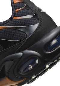 Chaussure de sport noire avec une tige texturée et des accents brillants, dotée d'un rembourrage à air visible et d'un détail orange sur le côté.