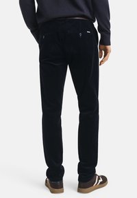 Pantalons en velours côtelé bleu marine à coupe droite, avec des poches arrière et un léger éclat ; associés à des baskets marron.