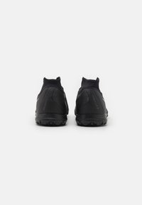 Zapatillas deportivas negras con un upper sintético liso, cuello tipo calcetín y suela de goma texturizada con tacos que proporcionan agarre.