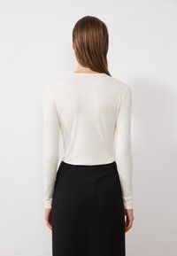 Långärmad, åtsittande topp i ett ribbat, off-white tyg, kombinerad med en högmidjad, svart kjol; slät textur och minimalistisk design.