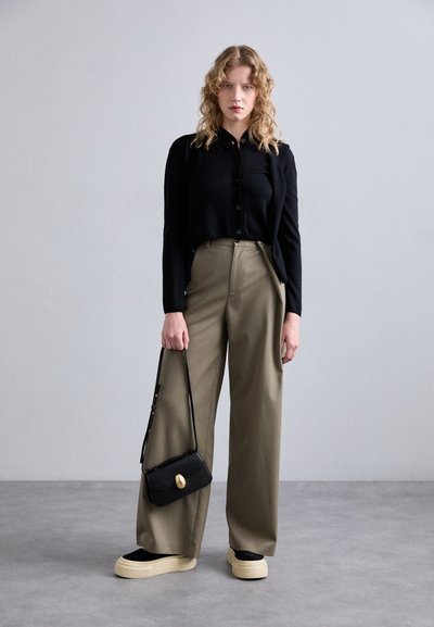 Black cropped cardigan, olive wide-leg trousers, black handbag with gold accent, and chunky black platform shoes with light sole.