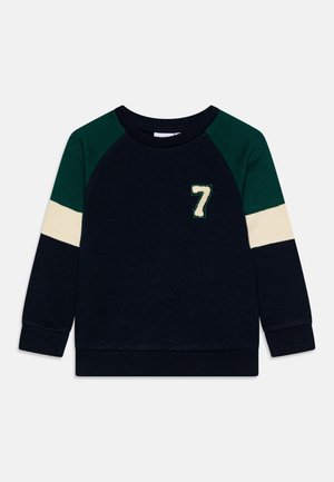 Sweat-shirt bleu marine avec des manches raglan vertes, une rayure horizontale crème et un numéro "7" brodé en blanc sur le devant. Texture douce, poignets côtelés.