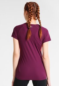 Skräddarsydd kortärmad träningsskjorta i djup lila med orange detaljer, med ett texturerat tyg och platta sömmar för komfort.