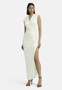 Abito bianco aderente con scollatura a V profonda, maniche a cappuccio, dettagli arricciati sui lati e uno spacco alto sulla coscia. Accentuato da una piccola hardware decorativa.
