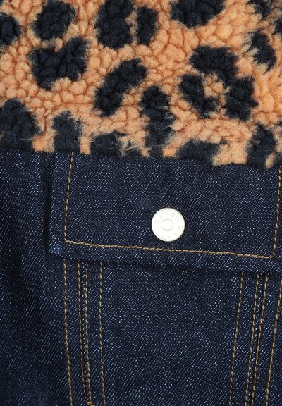 Tissu en jean de couleur bleu foncé, avec une partie supérieure en polaire imprimée léopard noir et marron. Comprend un bouton-pression argenté sur une poche avec des coutures jaunes.