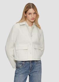 Veste en laine gris clair coupée, avec deux poches avant et de grands boutons. Présente un col et une texture douce. Assortie à un jean bleu.