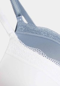 Sujetador con panel superior de malla azul, ribete de encaje floral, base blanca, tirantes ajustables y textura de tela suave y lisa.