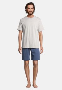 T-shirt in cotone grigio chiaro con maniche corte abbinato a pantaloni corti blu. Vestibilità casual, senza motivi o dettagli visibili. Indossato a piedi nudi.