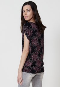 Haut noir à manches courtes avec un motif floral dans des nuances de rouge et de gris. Tissu lisse avec un détail de bas froncé.