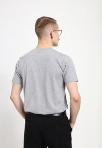 Šedé bavlněné tričko s krátkým rukávem, kulatým výstřihem a volným střihem. Nosené s černými kalhotami, které mají kapsy a opasek.