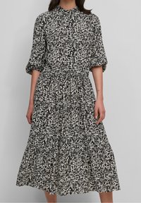 Zwart-witte jurk met patroon, hoge kraag, korte mouwen, getailleerde taille en een vloeiende rok die tot halverwege de kuit reikt.