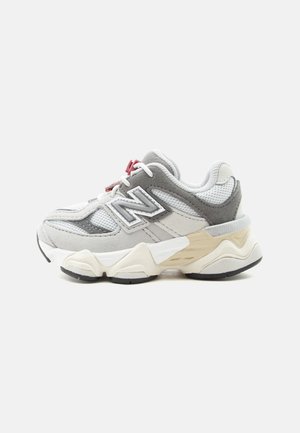 Basket en mesh gris et blanc avec empiècements en suède, semelle crème épaisse et verrou rouge sur les lacets, vue de côté sur fond blanc.