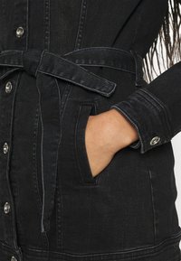 Černé deninové šaty s knoflíky a páskem. Mají kapsu v pase, kontrastní šití a strukturovaný límec.