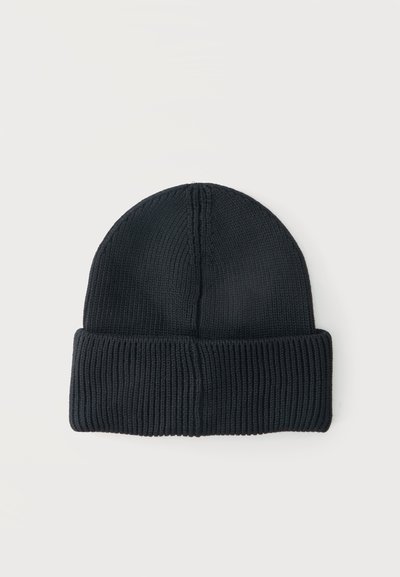 Bonnet en tricot noir avec bord replié sur un fond uni clair.