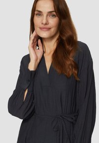 Schwarz gestreiftes Kleid mit V-Ausschnitt und langen Ärmeln. Mit einem Bindegürtel in der Taille und einem strukturierten, fließenden Stoff.