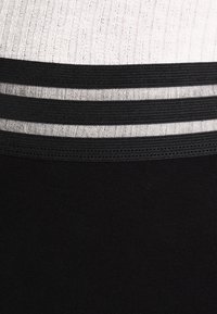 Primer plano de una tela acanalada en blanco y negro con dos bandas elásticas negras y dos rayas metálicas plateadas entre ellas.