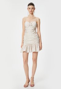 Vestido mini ajustado con estampado floral, fruncidos, tirantes de espagueti y dobladillo con volantes; presenta un detalle de nudo en el busto.