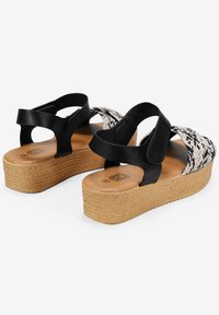 Sandalias de plataforma tejidas en negro y crema con suelas de corcho, que cuentan con correas elásticas y un upper texturizado para un ajuste seguro.