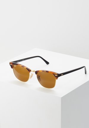Óculos de sol em padrão tartaruga com lentes castanhas, detalhes em metal e hastes pretas. Design de aro quadrado com detalhes clássicos e um visual minimalista.