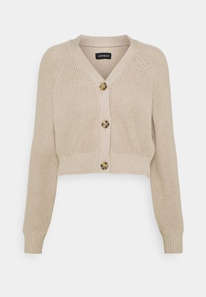 Béžový pletený krátký kardigan s výstřihem do V, třemi velkými knoflíky ve vzoru želvoviny, dlouhými rukávy a žebrovanými manžetami a lemem.
