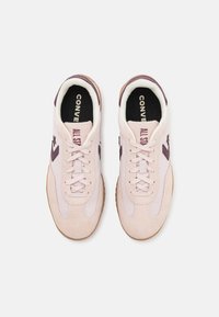Lyserød sneaker lavet af ruskind og mesh-materialer, med brune detaljer, gummisål, rund tå og snørelukning. Teksten på tungen siger "Converse All Star."
