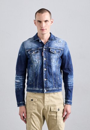 Chaqueta de denim en un degradado azul con un ligero desgastado y salpicaduras de pintura coloridas, con bolsillos frontales y acentos de hardware plateado.